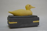 Side and top angled view showing the yellow duck on lid and overall box color and accents