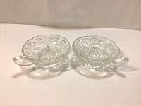 Pair of vintage clear glass candy bowls with one handle, viewed from above showing detailed pressed glass pattern and scalloped edges.