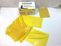Yellow thin latex resistance band laid out alongside its packaging and informational insert, showing the band and promotional material for TheraBand latex resistance bands.