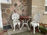 Full view of two white metal chairs and round bistro table with decorative scrollwork