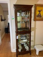 Front view of the wooden curio cabinet with glass shelves showing the upper and lower sections with glass doors, decorative carvings and contents inside (not included).