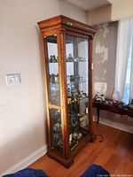 Full view of tall wood display cabinet showing front glass door and internal glass shelves with dark wood frame.