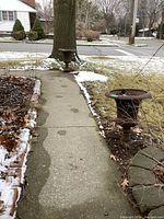 Photo showing two of three cast iron planters along a sidewalk, outdoors with some snow around them.