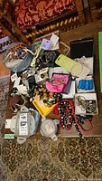 Photo showing assorted costume jewelry laid out on a surface, including bracelets, necklaces, rings, and boxed coins.