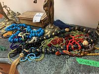 Beaded necklaces laid out on a surface with two small decorative boxes and part of a brass or bronze lamp stand visible.