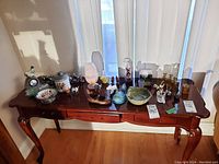 Photo of long wooden table with assorted figurines, bowls, jars, and glass bottles arranged on top showing the full lot