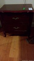 Front view of a dark wood night table with two drawers and brass handles, showing overall shape and condition.