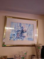 Framed watercolour print of flower bouquet hung on a wall with some glassware below.