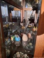 Display cabinet with various onyx, marble, and quail eggs along with silver plate decorative cups and small vases