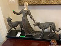 Front view of metal statue featuring woman and two dogs on black base, showing damage to hands.
