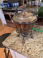 Front perspective of the tea pot set on its warming stand showing overall shape, lid, spout, and wood handle.