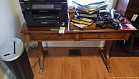 Wood table with two drawers and various items on top including printer, papers, calculator, and office accessories. Displays condition of table with visible wear and scratches.