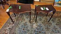 Two wood side tables placed on a patterned rug with visible scratches on their surfaces.