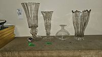 Four clear crystal vases on a shelf, different heights and designs, with readable auction tag.