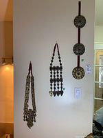 Three pieces of metal and rope wall art hanging on a beige wall showing their full form and relative sizes