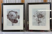 Two framed botanical flower prints with mirrored glass borders placed side by side. Each shows a different flower print. Frames have minor visible scuffs.