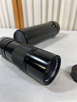 Canon Zoom Lens FD 100-200mm 1:5.6 S.C. lens alongside its black cylindrical carrying case and lens cap, showing lens body and zoom grip.