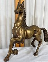 Front right side view of the brass horse in a rearing pose showing muscle details and raised foreleg.