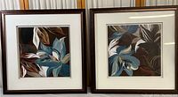 Two framed floral artworks side by side with blue and brown petals and leaves, dark wood frames, white mats.