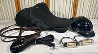 Full view of saddle, helmet, leather straps, and metal stirrups laid out on table