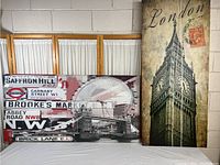 Photo showing two large London themed prints propped against a wall with a curtain background, one wide and short, the other narrower and taller.