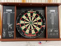 Front view of dartboard mounted in wooden cabinet with chalkboard scoring panels, visible chalk markings and wear.