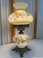 Full side view of the vintage hurricane lamp showing painted glass body, metal base, and ruffled top shade.