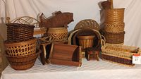 Collection of multiple wicker baskets of various styles and a small wooden shelf arranged on a table with white cloth background.