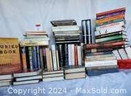 Wide view of stacks of various books in multiple piles on a table.
