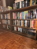 Two wooden bookshelves side by side filled with hardcover and paperback books, parquet floor visible