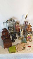 Wide view showing wooden candlesticks, marble candlesticks, glass display case with figurines, carnival girl figurine, wooden hand, and vintage matchboxes in copper lantern.