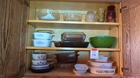 Wood cabinet shelf showing variety of bowls and dishes including Corningware, mixing bowls, glass casseroles, and drinking glasses.