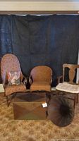 Overall lot showing two wicker chairs, solid wood chair, storage chest, vintage gramophone horn, and decorative pillow