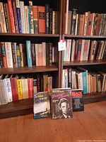 Two books in front of a bookshelf filled with hardcover and paperback theatre-related books. Titles visible include "The Track of the Cat," "Good Night Sweet Prince," and others.