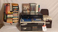 Samsung DVD-VR375 DVD recorder and VCR unit atop its retail box. To the left and right are several stacks of VHS tapes in cardboard boxes and a dark container.