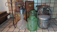 Wide view showing glass decanter, green canisters, metal ice bucket and wooden boxes in background with wire mug tree