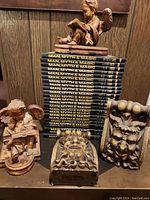 Stack of 24 Man, Myth & Magic hardcover volumes with two angel bookends and two demon gargoyle wall hangings in front.