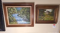 Two framed original outdoor landscape paintings on a wall, showing the Mountain Stream and Farmhouse scenes.
