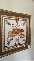 Full view of framed silk scarf featuring a large golden carriage on a white background with maroon and gold decorative borders.