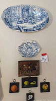 Full view of all items displayed on wall: two platters, four small fruit paintings, carved wood kitchen scene