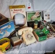 Two vintage rotary dial telephones, a Futuristic Heating heating pad box, Ronco cordless broom box, and other items arranged on tabletop