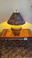 Wood coffee table with metal base supporting a leather-covered lamp with a large irregular dark leather lampshade, lamp is illuminated.