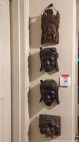 Four wooden hanging masks mounted vertically on a wall showing different styles and sizes.