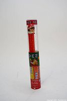 Front view of the Pez Christmas candy dispenser featuring the elf head and red stem in its plastic packaging