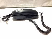 Side view of vintage black telephone with coiled handset cord and telephone line cable showing RJ11 connector.