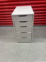 Front view of the 5 drawer white melamine cabinet showing all drawers closed, straight on against a red background.