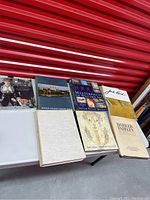 7 hardcover art and coffee table books arranged side by side on white table against red background.