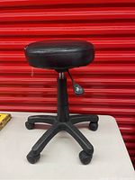 Front-side view of black adjustable rolling stool showing padded round seat and five caster wheels base