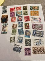 Photo showing a collection of 29 vintage stamps on white paper from countries including Canada, USA, Bahamas, South Africa, Italy, and Denmark, with various designs and cancellation marks.