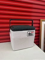 Photo of white and green Coleman Super Oscar cooler with handle, angled view showing front and side.